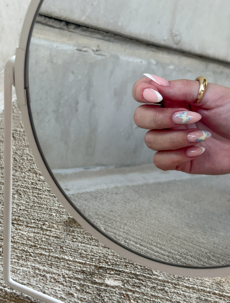 french manicure with blue butterfly design in a mirror reflection